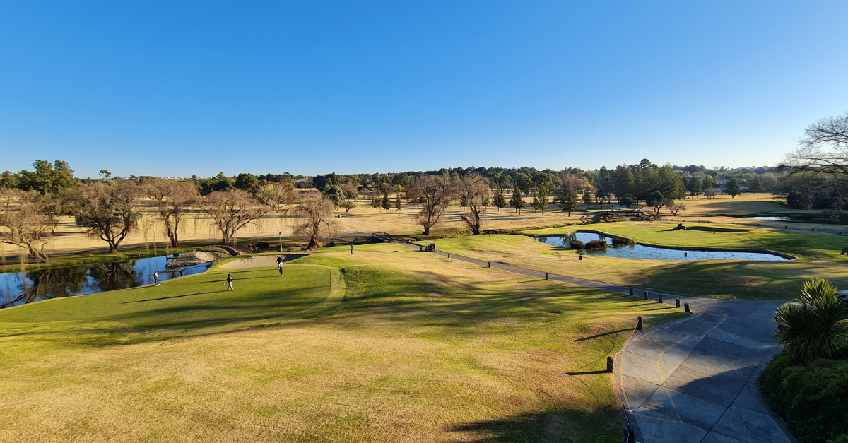 A scenic view of Modderfontein Golf Club's lush green fairways under a clear Johannesburg sky