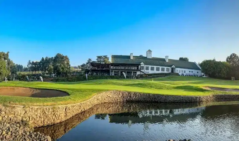 Scenic view of the Modderfontein Golf Course clubhouse and green reflecting in a pond under a clear blue sky.